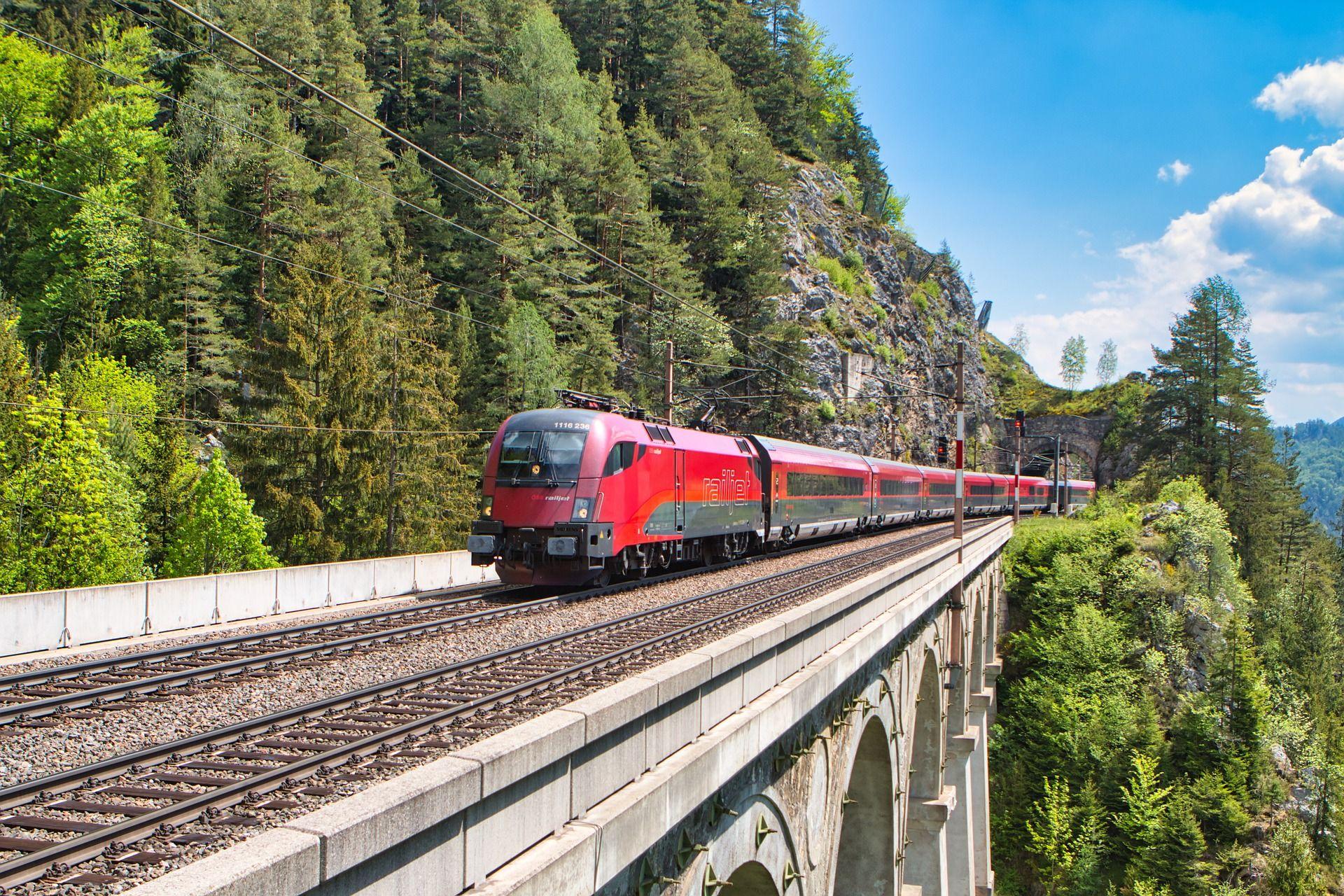 Roter Zug fährt über Brücke, Wald im Hintergrund